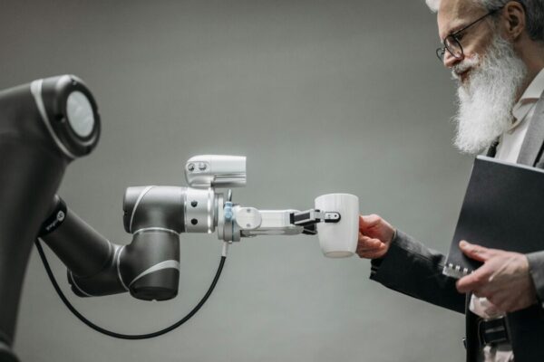 An elderly man receives a cup from a robotic arm in a modern office setting. &mdash; Photo by Pavel Danilyuk on Pexels