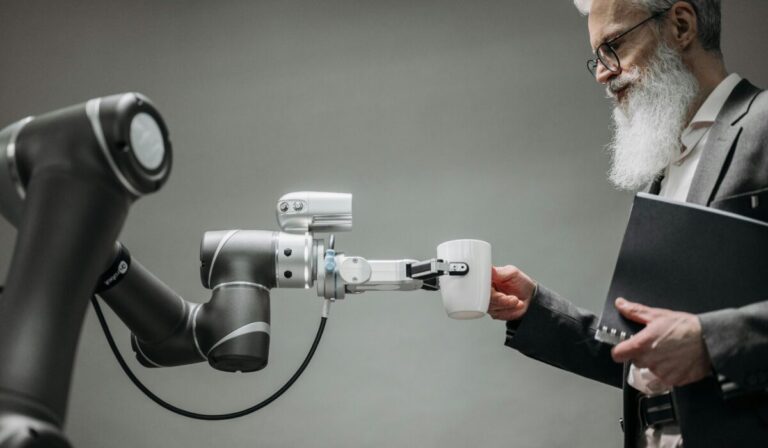 An elderly man receives a cup from a robotic arm in a modern office setting. &mdash; Photo by Pavel Danilyuk on Pexels
