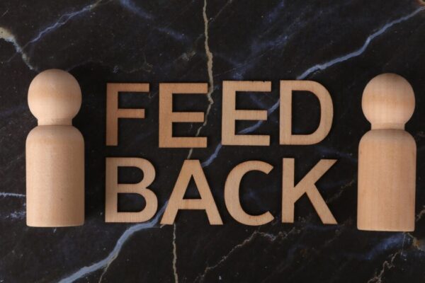Wooden letters spelling 'Feedback' with peg-like figures on marble background. &mdash; Photo by Ann H on Pexels