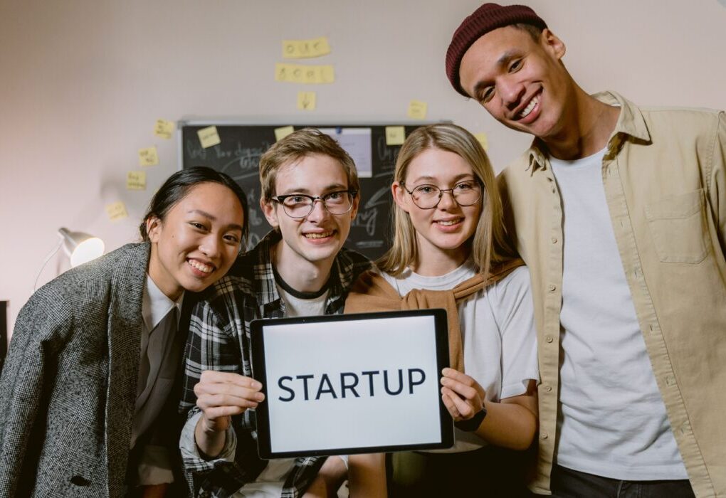 A diverse group of young professionals in a startup office, smiling and holding a sign. &mdash; Photo by Tima Miroshnichenko on Pexels