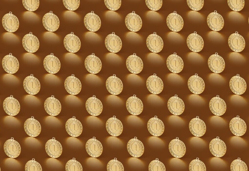 Multiple gold medals arranged in a repeating pattern on a brown backdrop. &mdash; Photo by DS stories on Pexels
