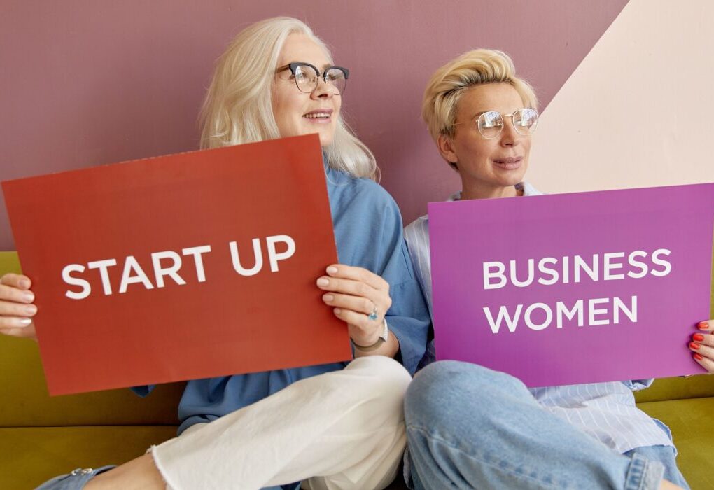 Two women on a sofa holding signs promoting startup and business women. &mdash; Photo by Darina Belonogova on Pexels